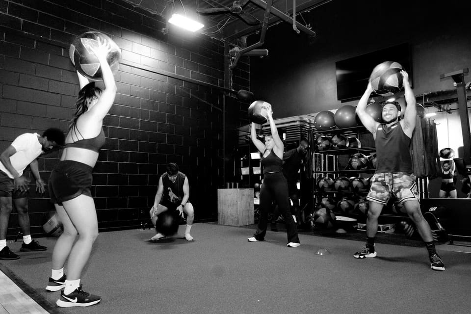 Members pressing medicine balls overhead during a group class at Kinetic Haus